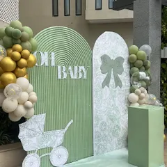 A modern and chic 'Oh Baby' shower setup in a lovely sage green. The decor features clean, arched backdrops with different textures and delicate line-art graphics of a bow and a baby carriage.