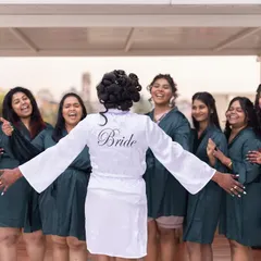 A fun and candid moment between the bride and her bridesmaids, all in matching robes, sharing a laugh before the ceremony.