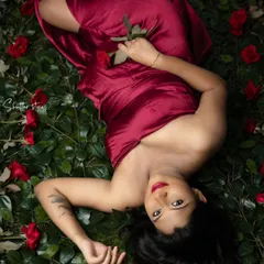A bold and artistic maternity portrait. Lying on a bed of green leaves with red roses, this mom-to-be looks absolutely stunning in a flowing red satin wrap.
