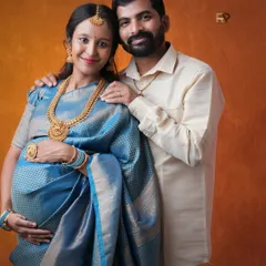 A stunning portrait of a mom-to-be in a traditional blue silk saree, adorned with classic temple jewelry. The warm, earthy backdrop complements the richness of her attire.