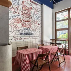 We brought a burger brand's playful personality to life with a custom, large-scale wall mural that serves as the centerpiece of the diner. Paired with classic red-and-white gingham tablecloths and simple wooden chairs, the design creates a fresh, modern take on retro American diner aesthetics.