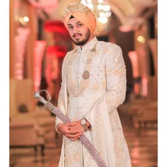 A portrait of a Sikh groom in his white and gold sherwani, holding a traditional kirpan. The image exudes regal elegance and cultural pride.