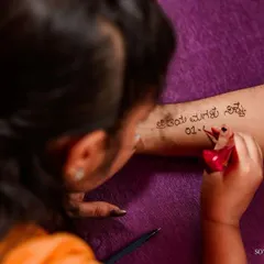 A close-up of a father getting his daughter's wedding date written on his arm in henna. A beautiful, personal gesture of love.