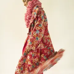 An editorial look for Vogue featuring a layered ensemble with a floral coat and a textured pink floral collar. The motion blur on the hem of the coat adds a dynamic quality, highlighting the rich textures and patterns of the designer pieces.