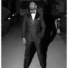 A dapper black and white portrait of the groom in a classic double-breasted tuxedo, captured at night with dramatic lighting that creates a strong shadow.