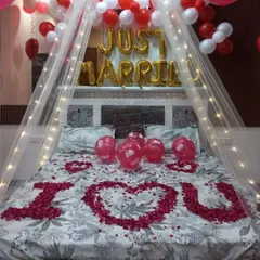 A classic 'Just Married' room decoration to welcome the newlyweds. I used a canopy with fairy lights, 'Just Married' foil balloons, and a heart shape made of rose petals on the bed for a truly romantic atmosphere.