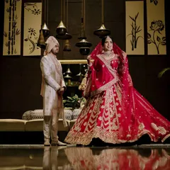A classic wedding portrait that captures the grandeur of the day. The bride's magnificent red lehenga and the groom's regal sherwani are framed perfectly, creating an iconic image for the couple to cherish.