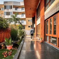A covered walkway alongside the Hennur residence, with a reflective granite floor that mirrors the sky and the home's warm wooden ceiling.