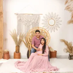 A full view of my boho-themed studio setup, featuring a wicker peacock chair, macrame hangings, and dried grasses. The couple's soft pink and blue outfits complement the natural tones.