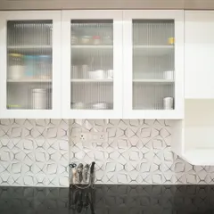 A close-up of white upper cabinets with fluted glass doors, set against a unique 3D geometric tile backsplash. This combination adds layers of texture and modern style to the kitchen.
