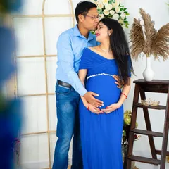 A tender moment captured in our studio. The partner places a gentle kiss on the mom-to-be's forehead as they both hold the baby bump, dressed in coordinating blue outfits.