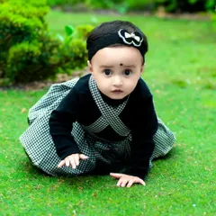 A sweet baby girl looking directly at the camera during her outdoor portrait session. The vibrant green lawn makes her stand out, creating a classic and heartwarming baby photo.