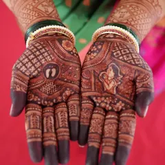 A beautiful baby shower mehendi with a rich, dark stain. The design includes a portrait of a mother holding her baby and tiny baby footprints on the other palm.