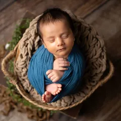 A classic potato sack pose, where the baby is wrapped snugly to feel secure and sleepy. The deep blue wrap provides a beautiful pop of color against the rustic backdrop.