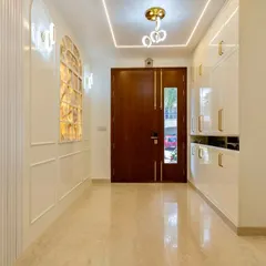 This elegant foyer blends modern design with classic charm. The illuminated onyx wall feature, glossy white cabinetry with gold accents, and warm marble flooring create a sophisticated and welcoming first impression.