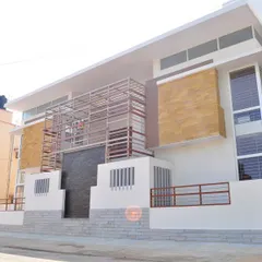 The Prabhakar Residence in Bangalore presents a modern exterior with a mix of materials, including white plaster, stone cladding, and metal screening. The design creates a layered and textured facade that is both contemporary and visually engaging.