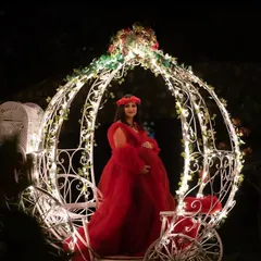 A true fairytale moment. This outdoor night shot features the mom-to-be in a red gown, seated in a beautifully lit Cinderella carriage, creating a magical and unforgettable image.