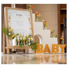 The welcome setup for the "Baby in Bloom" shower. It features a custom sign on a wooden easel, bold "BABY" letters, and a beautiful arrangement of fresh, colorful flowers.
