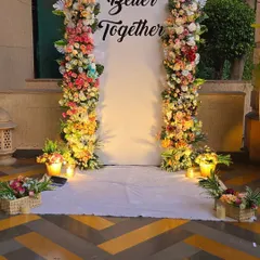 A wide shot of the floral "Better Together" backdrop, showing how it creates an elegant and romantic focal point for photos. The warm uplighting enhances the colors of the flowers.