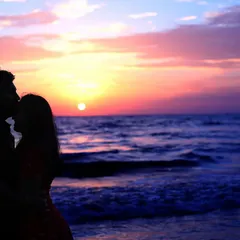 A silhouette of a couple against a breathtaking sunset over the ocean. This intimate pre-wedding photograph captures a tender forehead kiss, symbolizing love and gratitude.