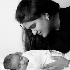 A tender black and white moment between a mother and her sleeping newborn. The soft lighting and her gentle gaze create a peaceful and loving atmosphere.