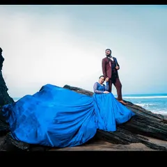 A dramatic pose on the rocks by the sea. The expansive blue trail of the gown contrasts with the natural landscape, making for a stunning pre-wedding photograph.