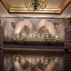 This stage reflects modern artistry with its sculptural white panels and a mountain of lush, pastel florals. The glossy, reflective floor doubles the visual impact, creating a dreamy and sophisticated atmosphere for a wedding reception.