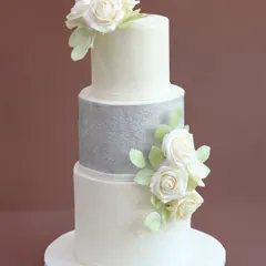 For a truly timeless celebration, this white and silver tiered cake combines classic elegance with modern texture. Each sugar flower is handcrafted petal by petal, creating a sophisticated look for a wedding or grand milestone.