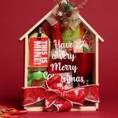 This adorable house-shaped wooden box is filled with Christmas goodies, including a festive drink, snacks, and a red goblet, all tied with a reindeer-themed ribbon.