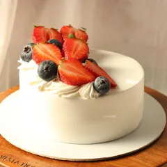 A close-up of the fresh berry cake, showing the juicy strawberries and blueberries on a bed of light whipped cream.