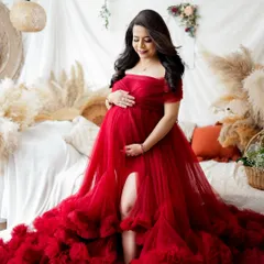 A stunning portrait of a mother-to-be in a vibrant red tulle gown. The boho-chic studio setup with pampas grass and soft lighting creates a warm and romantic atmosphere.