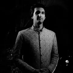 A powerful groom's portrait in black and white. The dramatic lighting creates a striking, classic look that emphasizes his sharp features and traditional attire.
