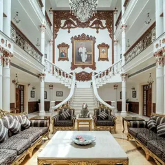 The heart of "The Palace Promised," this triple-height living room features ornate furniture, gilded accents, and a grand staircase backdrop, creating a space that is both magnificent and welcoming.