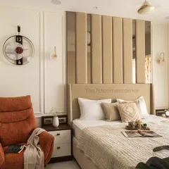 A wider view of the bedroom, showing the plush burnt-orange lounge chair that creates a cozy reading nook. The neutral tones and warm ambient lighting contribute to a comfortable and modern space.