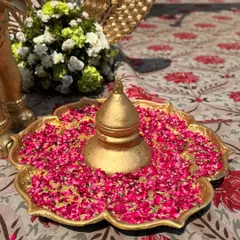 A traditional golden urli filled with water and vibrant pink rose petals, a classic decor piece that symbolizes prosperity and beauty in Indian culture.