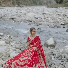A serene portrait of the bride sitting on a rock by the river, her red lehenga a vibrant splash of color.