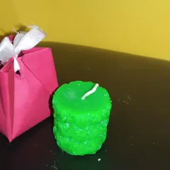 A textured green candle shown next to a small, handmade gift bag. This shows how my decorative candles can be packaged to make a thoughtful and unique present.
