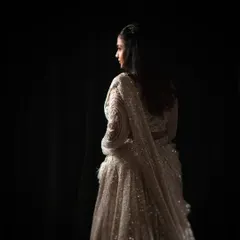 A study in light and shadow. This portrait uses a single light source to sculpt the bride's form and the beautiful texture of her lehenga, creating a sense of mystery and elegance.