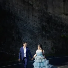 A candid shot of a couple walking hand-in-hand on a road in Bali. The focus is on their natural interaction and the beautiful, dramatic landscape surrounding them.