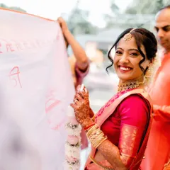 A candid moment from a beautiful South Indian wedding. The bride's smile says it all. Her makeup is kept fresh and luminous to complement the vibrant pink Kanjeevaram saree, paired with a classic bridal updo.
