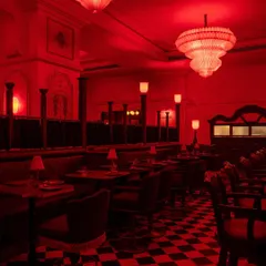 The main dining room, bathed in an intense red light. The checkerboard floor and ornate chandeliers create a sense of dramatic grandeur, a stage set for a memorable culinary performance.