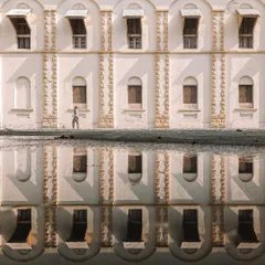 A creative composition showing a building and its perfect reflection in a puddle. A person walking by is also reflected, creating a symmetrical and surreal image that plays with perception.