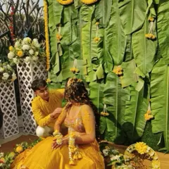 A classic Haldi moment with a backdrop of fresh banana leaves and marigold garlands. The bride, dressed in yellow, is seated for the rituals, creating a picture of tradition and joy.