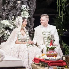 A beautiful moment captured at the mandap, where the couple sits before a magnificent Ganesha sculpture. The decor features a canopy of white flowers and hanging floral strings, creating a serene and blessed atmosphere for their wedding vows.
