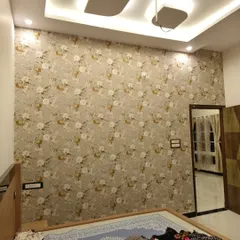This delicate floral wallpaper with a neutral color palette brings a soft, romantic feel to a bedroom. It covers the entire wall, creating a cohesive and serene backdrop that complements the room's lighting and decor.