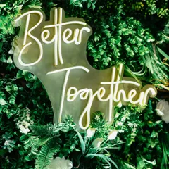 A custom neon sign saying "Better Together" nestled in a lush green floral wall. It's these personalized details that make a wedding feel unique.