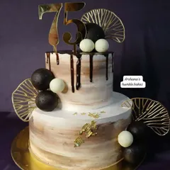 A sophisticated two-tiered cake for a 75th birthday celebration. The chocolate drip and gold accents add a touch of class.