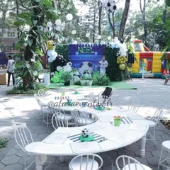An outdoor soccer-themed birthday party for a 6-year-old. The setup includes custom-designed tables, a large backdrop with the birthday boy's name, and a bouncy castle in the background for extra fun.