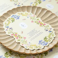 A beautiful brunch information card placed on a rustic plate. The card features a delicate, laser-cut shape and a border of hand-painted wildflowers, perfectly matching the garden party theme.