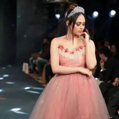A candid moment on the runway. The soft lighting catches the layers of the pink tulle gown, showcasing the movement and texture of the fabric as the model walks.